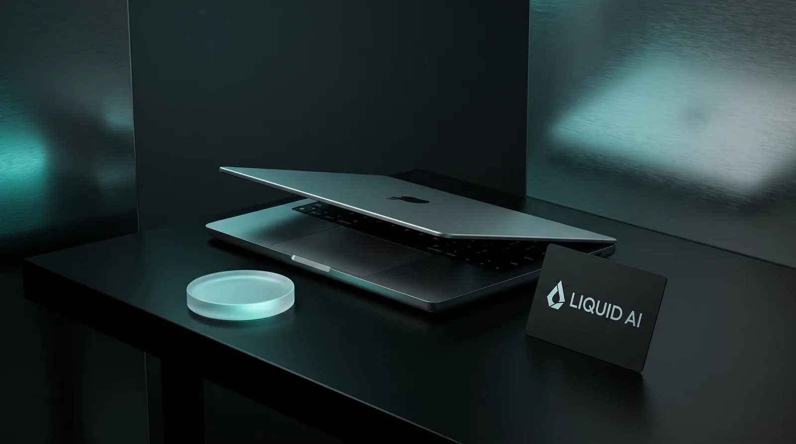 A thin silver laptop on a dark desk beside a glowing cyan glass disc and a black card carrying the Liquid AI wordmark