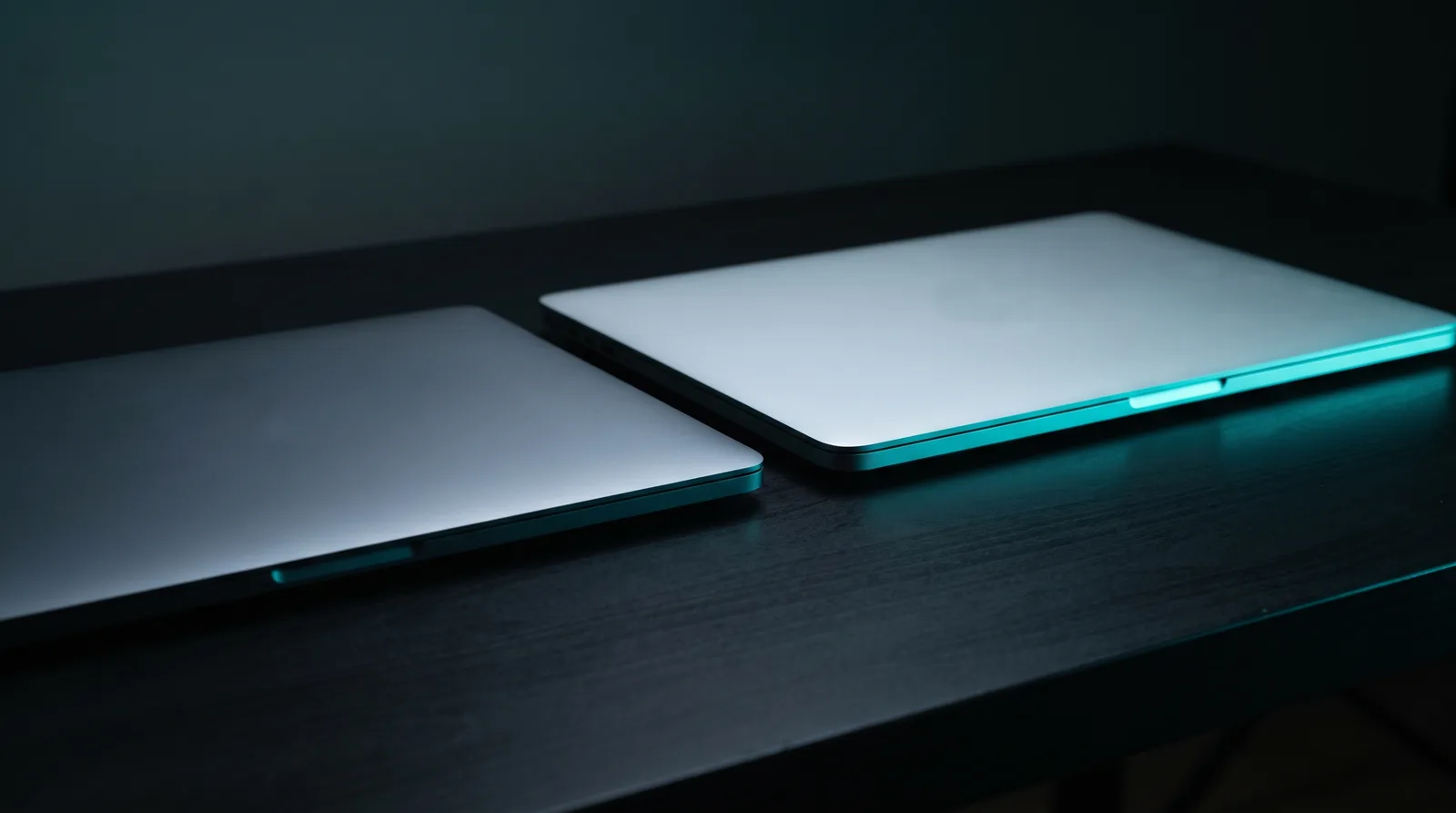 Two identical laptops side by side on a dark desk, one lit brighter than the other, the 24GB versus 48GB choice